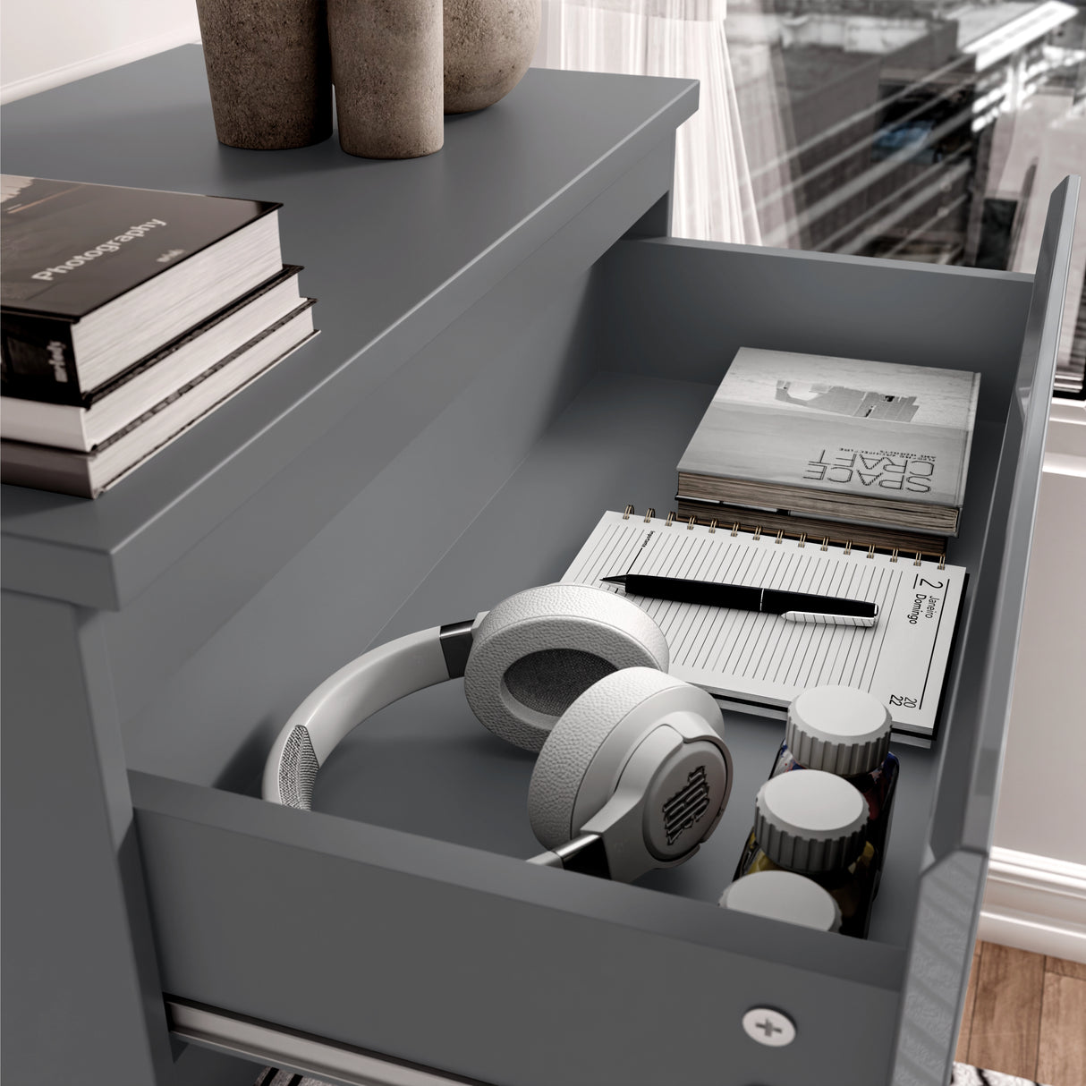 Open drawer for headphones, notebook, and pen on a dark grey surface.