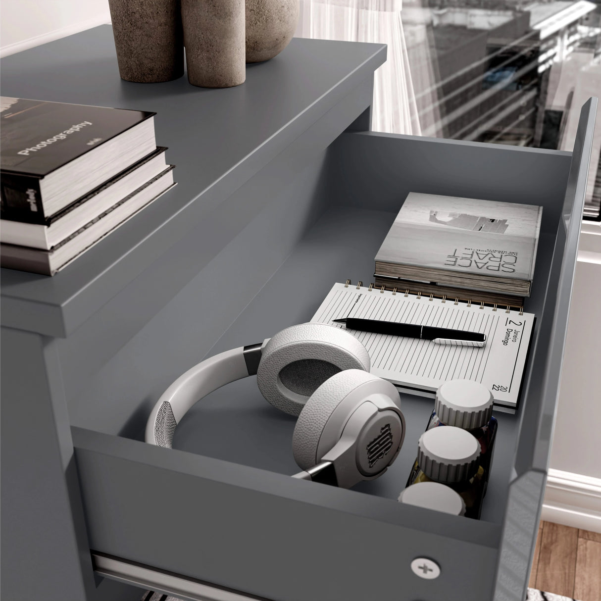 Open drawer for headphones, notebook, and pen on a dark grey surface.
