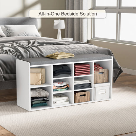 Hallway shoe storage bench with cushion and adjustable shelves placed at the foot of a bed, featuring multiple cubbies for shoes and folded clothes.