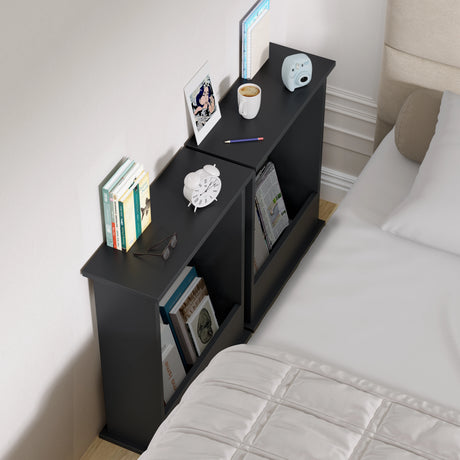 Black nightstand with books, a cup, and other items next to a bed.