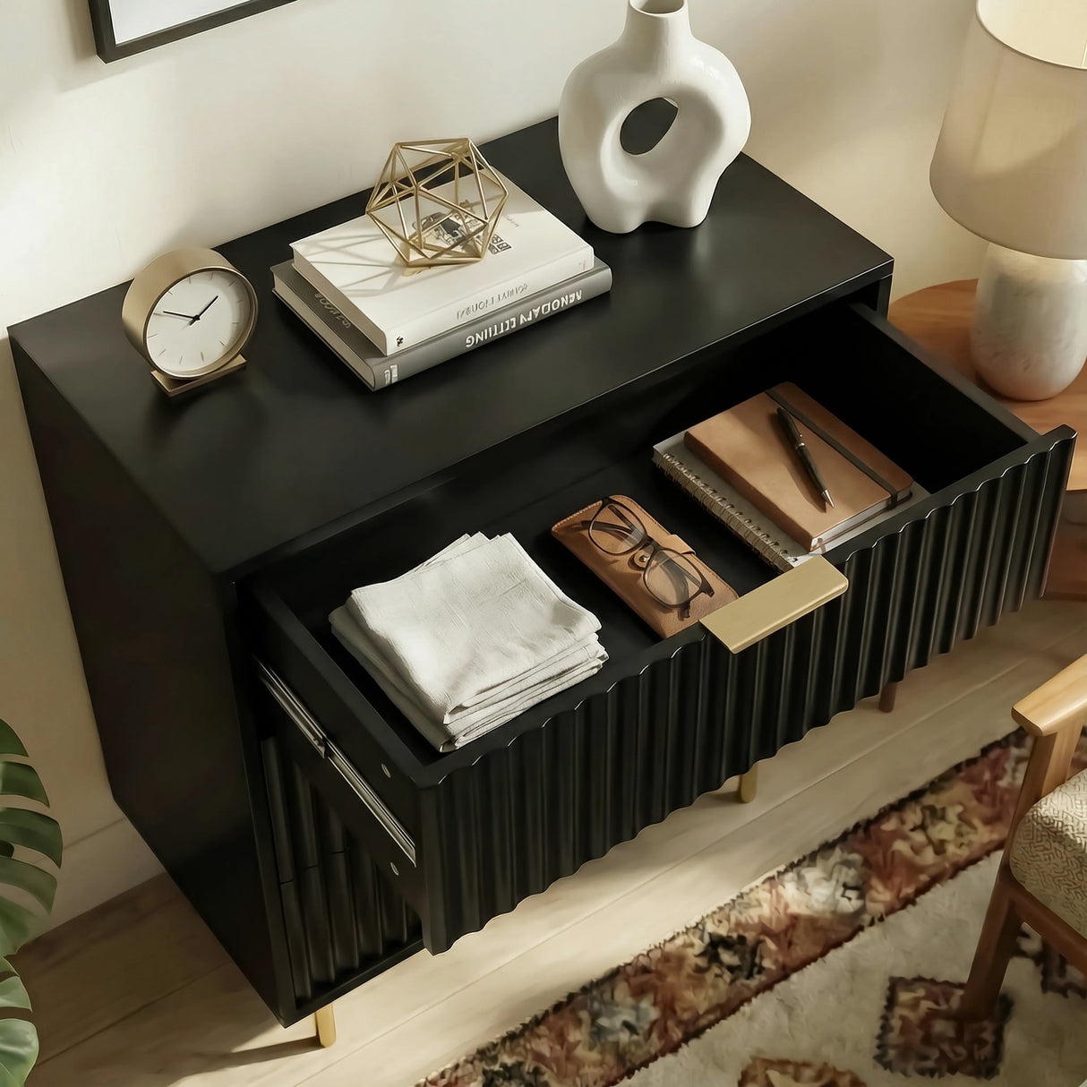 Black bedside table unit beside a bed, shown with an open drawer containing organised storage
