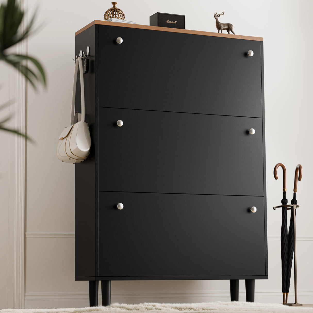 Tall three door black shoe cabinet with oak top and bag on side hook, two knobs per drawer in traditional-modern style.