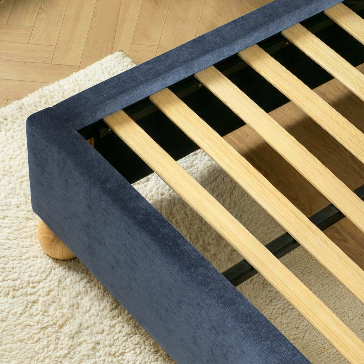 Close view of evenly spaced wooden slats set inside a blue upholstered king size bed frame for mattress support