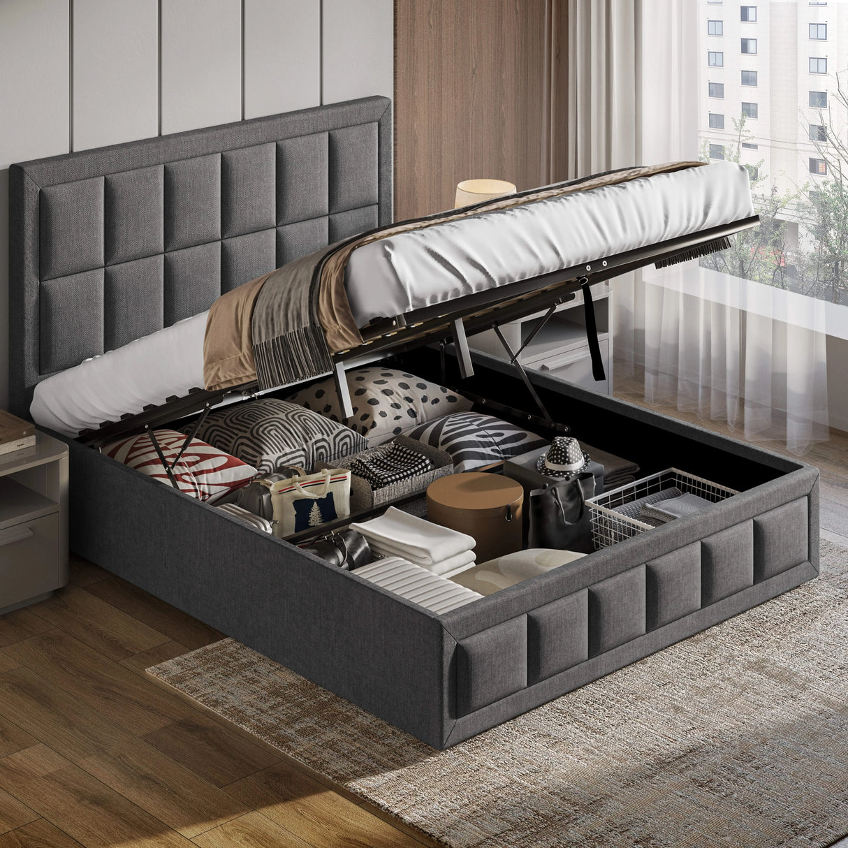 Gray upholstered bed with storage compartment open, revealing various items, in a room with wooden flooring and a window.