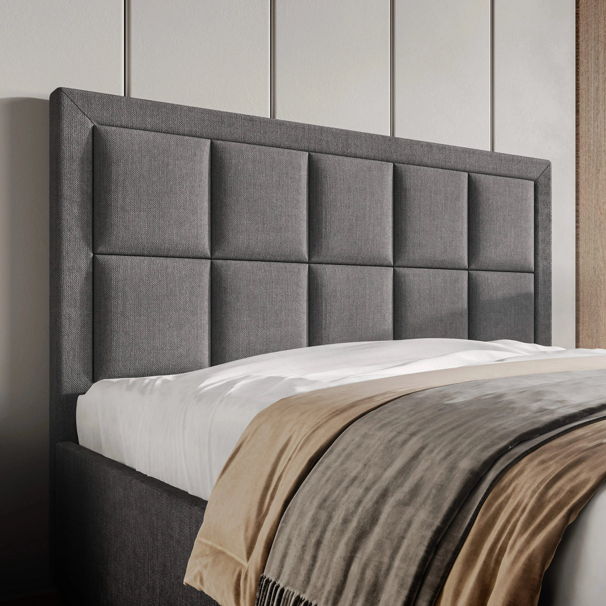Gray upholstered headboard with a bed and beige blanket in a bedroom setting.