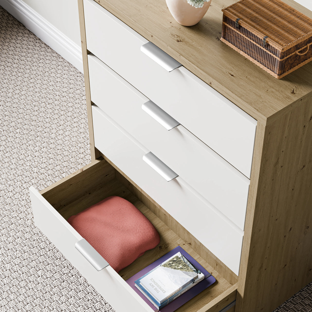 Wooden, white-finished deep chest of drawers with a lower drawer open, displaying folded clothes against a wall