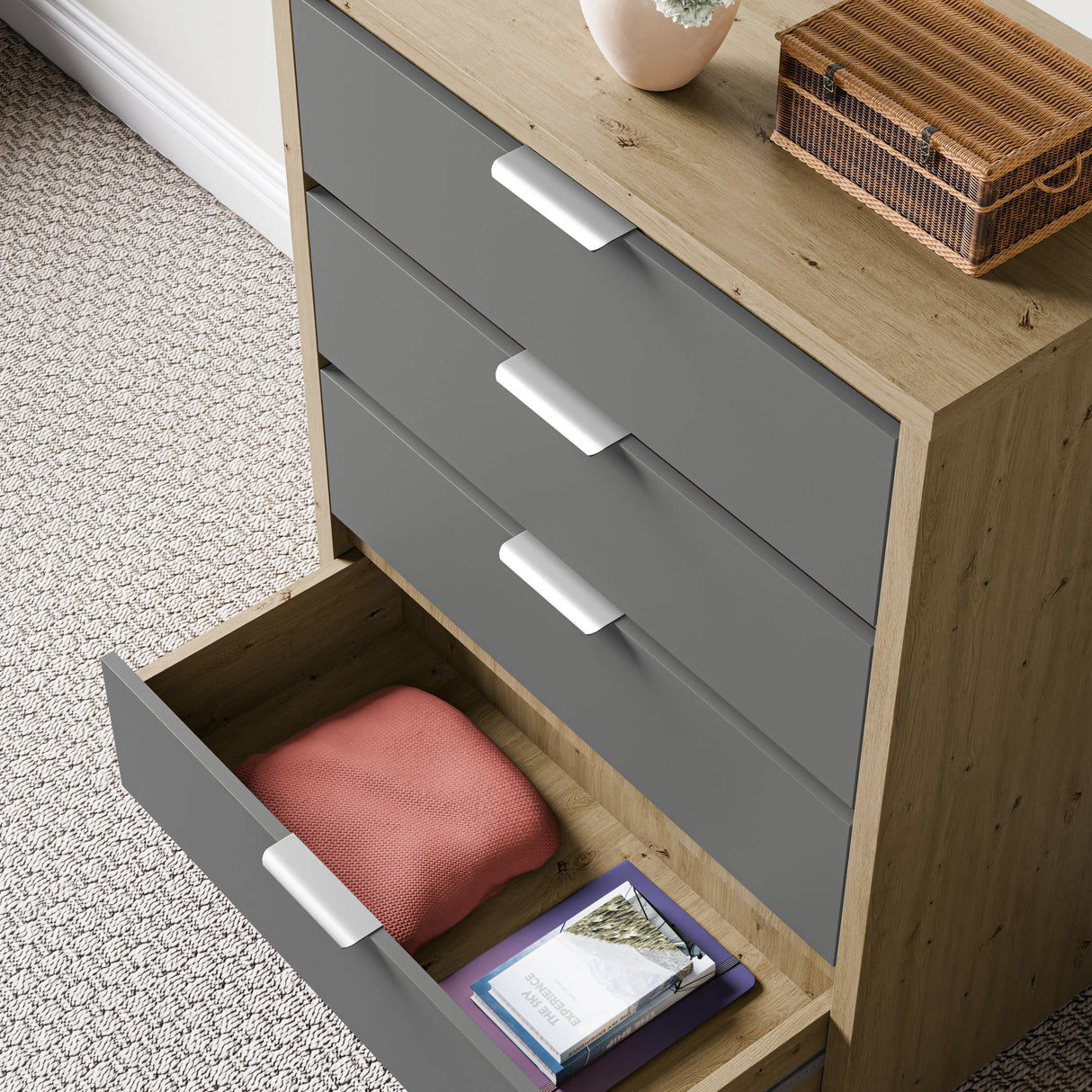 Wooden-grey finish deep chest of drawers with a lower drawer open, showing folded cloth and books placed against a wall