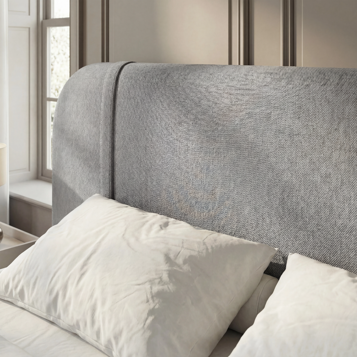Close detail of curved padded headboard in textured grey fabric upholstery in a natural light space