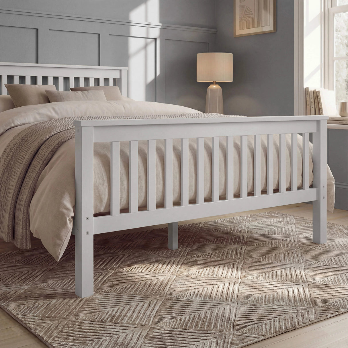 White double bed frame with slatted rails, neutral bedding, and a rug placed beneath in a natural light room