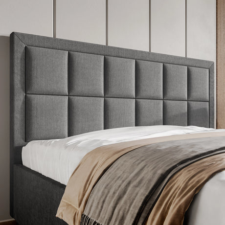 Gray upholstered headboard with a bed and beige blanket in a bedroom setting.