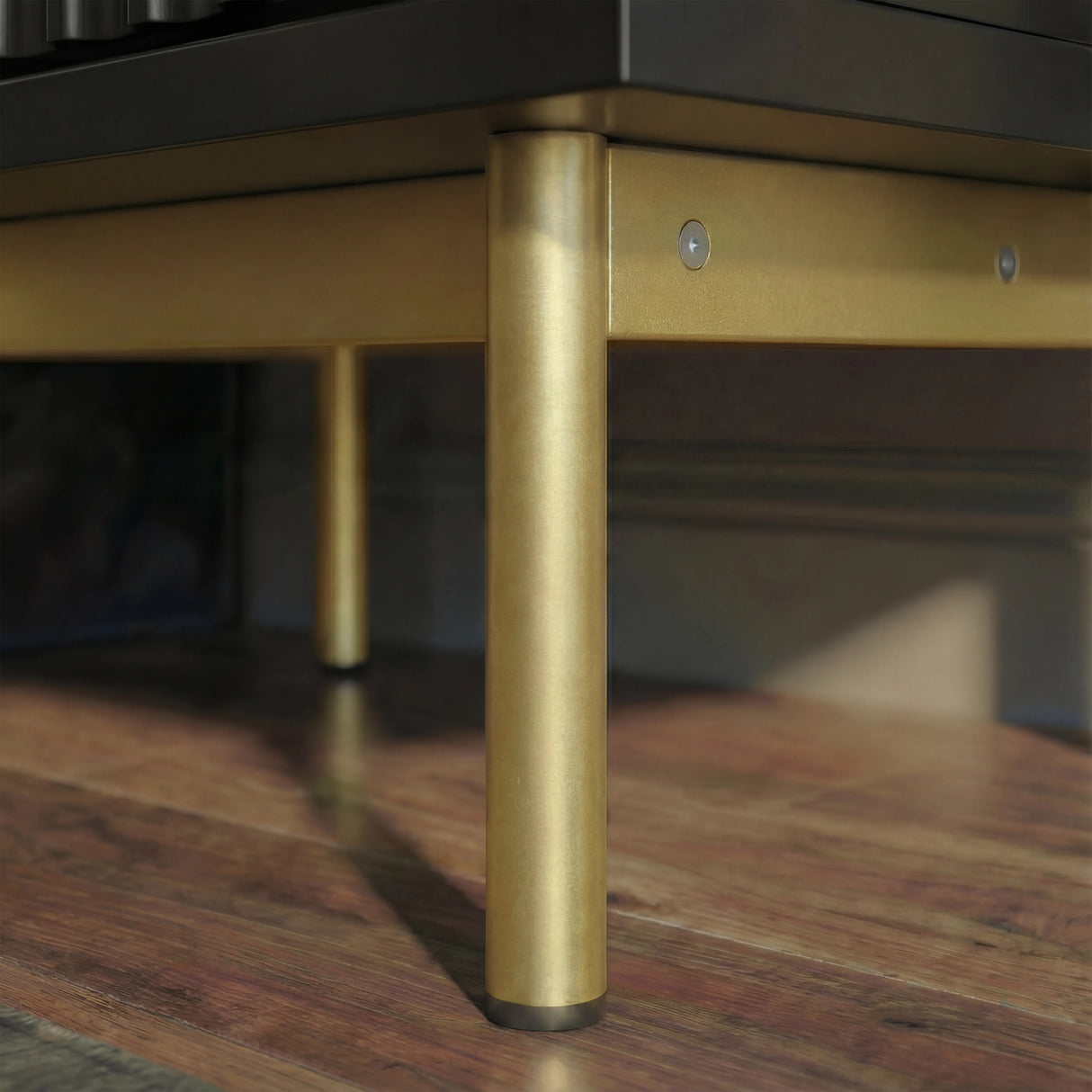 Black bedside cabinet lower corner with raised golden metal legs and structured base placed on a wooden flooring