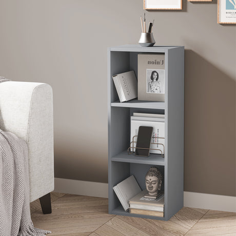 angled front view of 3 tier grey narrow shelving unit holding books and decor, ideal for tight spaces