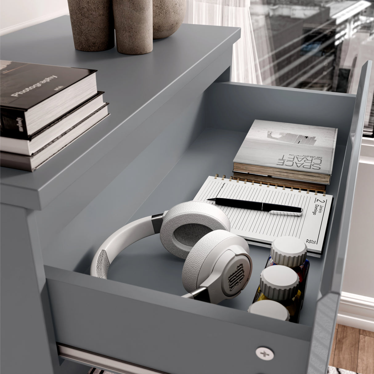 Close-up of drawer in grey high gloss chest, displaying storage for headphones, books, and personal items.