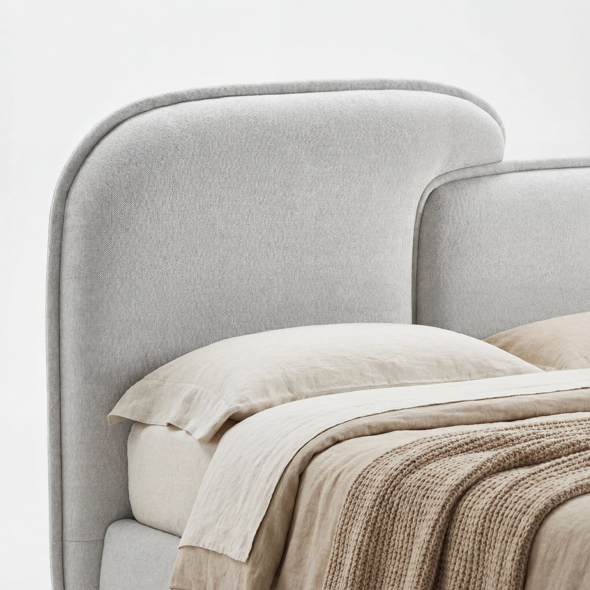 Close view of a softly curved, split-style padded headboard in grey fabric with subtle fabric texture