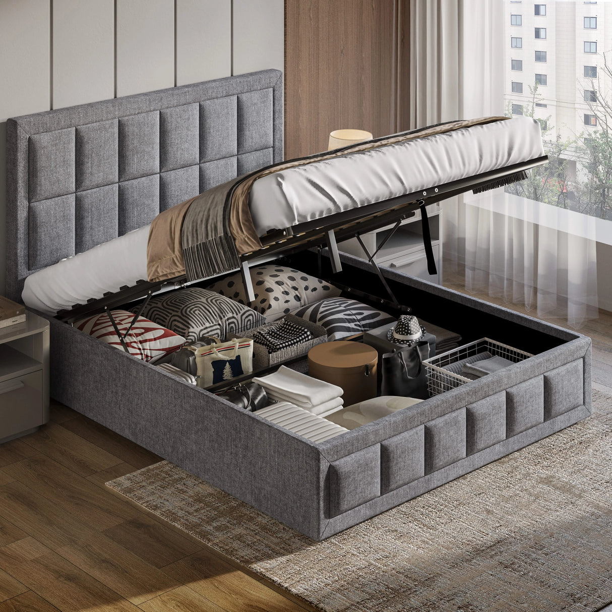 Gray upholstered bed with storage compartment open, revealing various items, in a room with wooden flooring and a window.