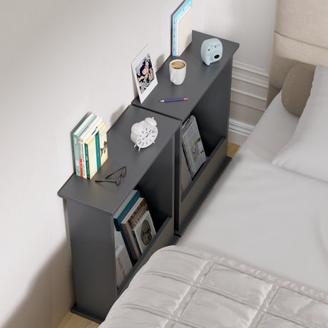 Gray nightstand with books, a cup, and other items next to a bed.