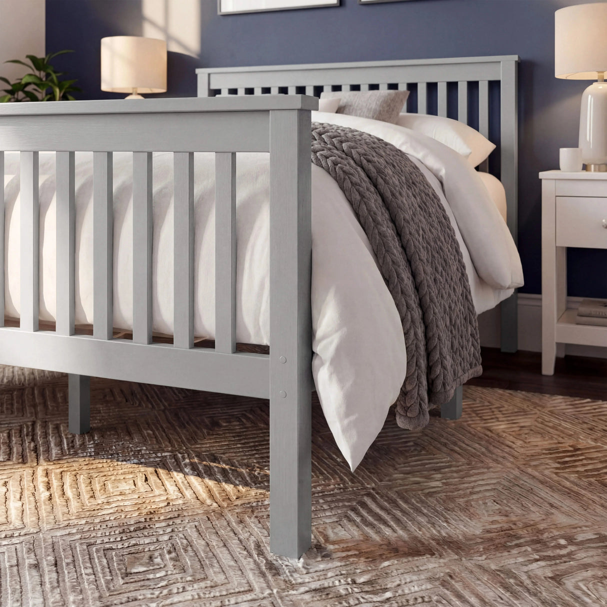 Grey wooden double bed frame with slatted rail pattern and layered bedding, placed in a natural light room