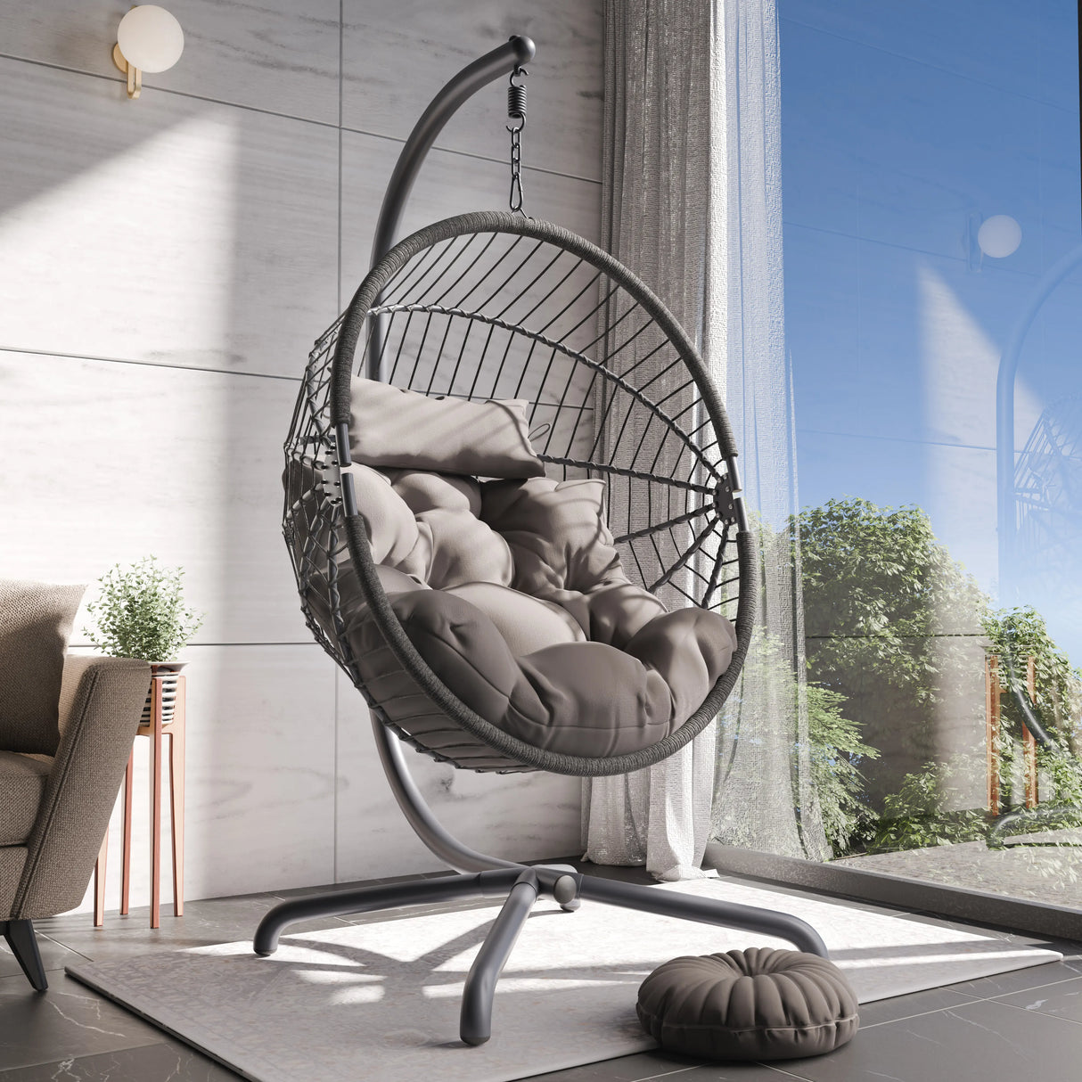 Hanging egg chair with cushions in a modern room with large windows.