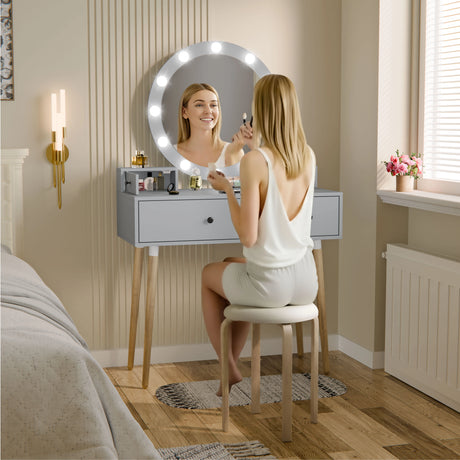Woman applying makeup in front of a vanity mirror with lights in a bedroom setting.