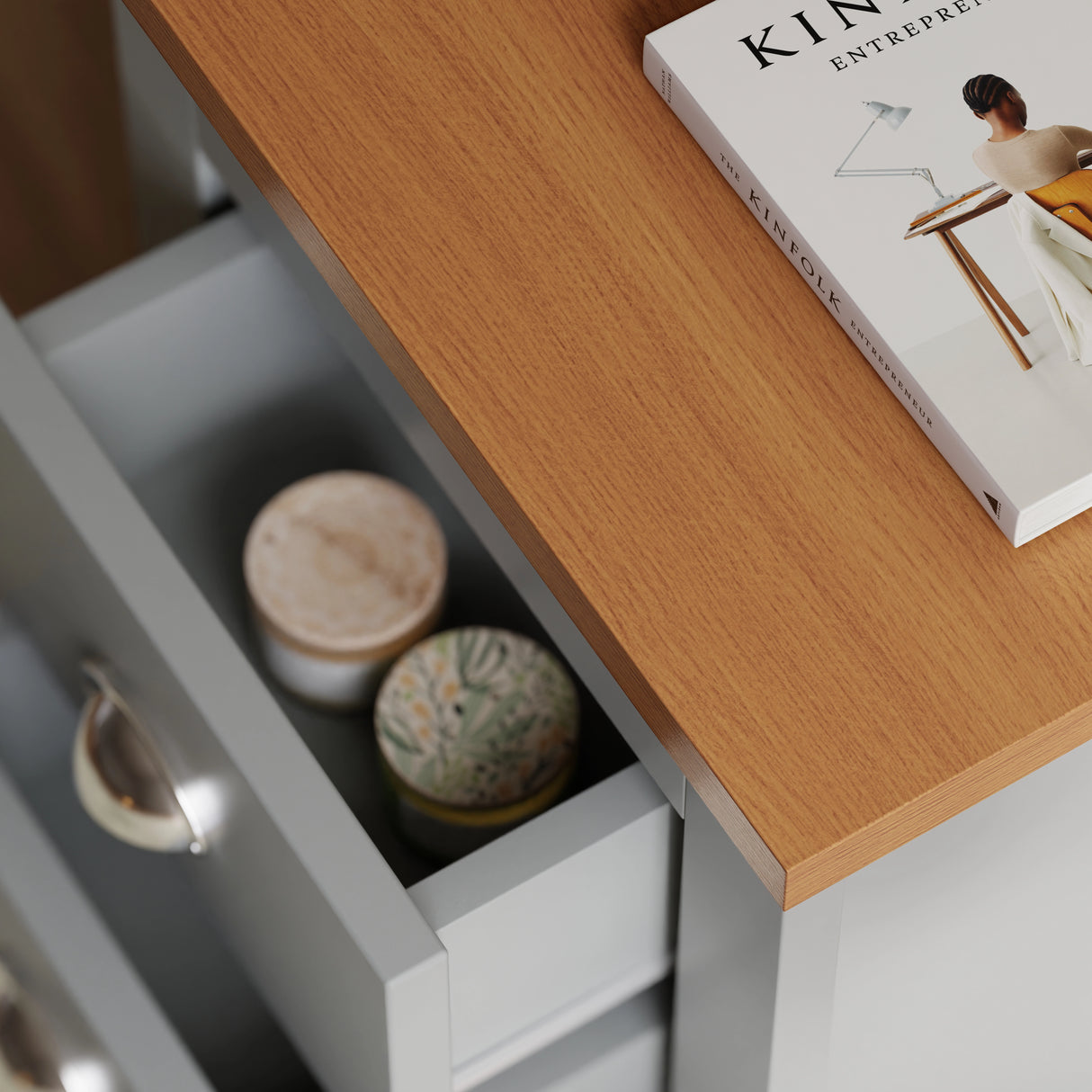 Close-up of oak-look top and open drawer of grey bedside table showing interior with candles and a book on top.