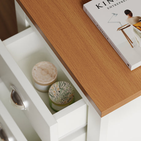 Close-up of oak-look top and open drawer of white bedside table showing interior storage with candles and book.