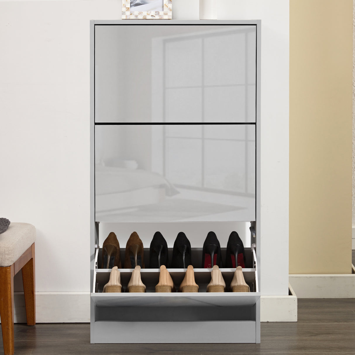 Front-facing thin shoe cabinet with the lowest drawer open, displaying multiple pairs of shoes.