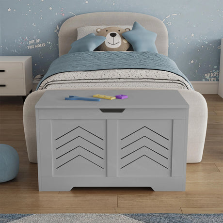 Grey toy storage box in a child's bedroom with a bed and teddy bear in the background.