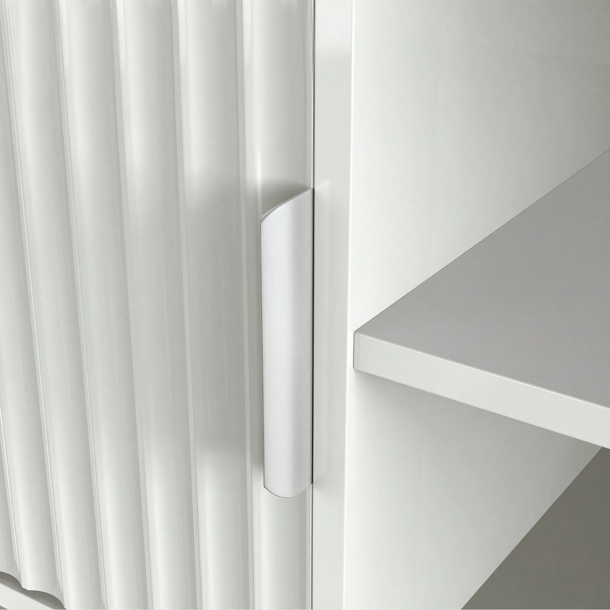 Sleek white TV media unit with vertical ribbing and silver handle, styled with books and minimalist home decor.