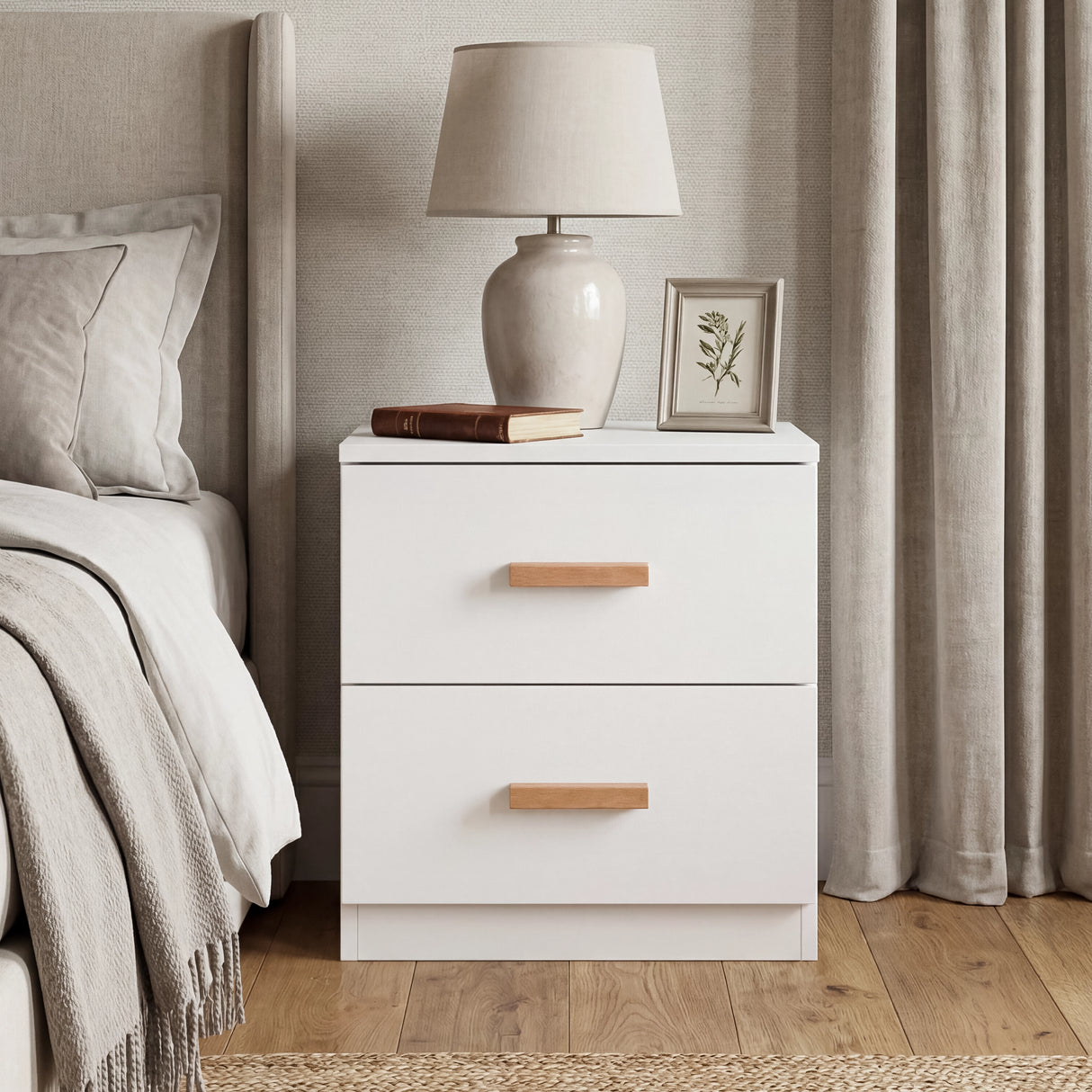White two drawer bedside table placed beside bed with wooden handles and neutral bedroom decor