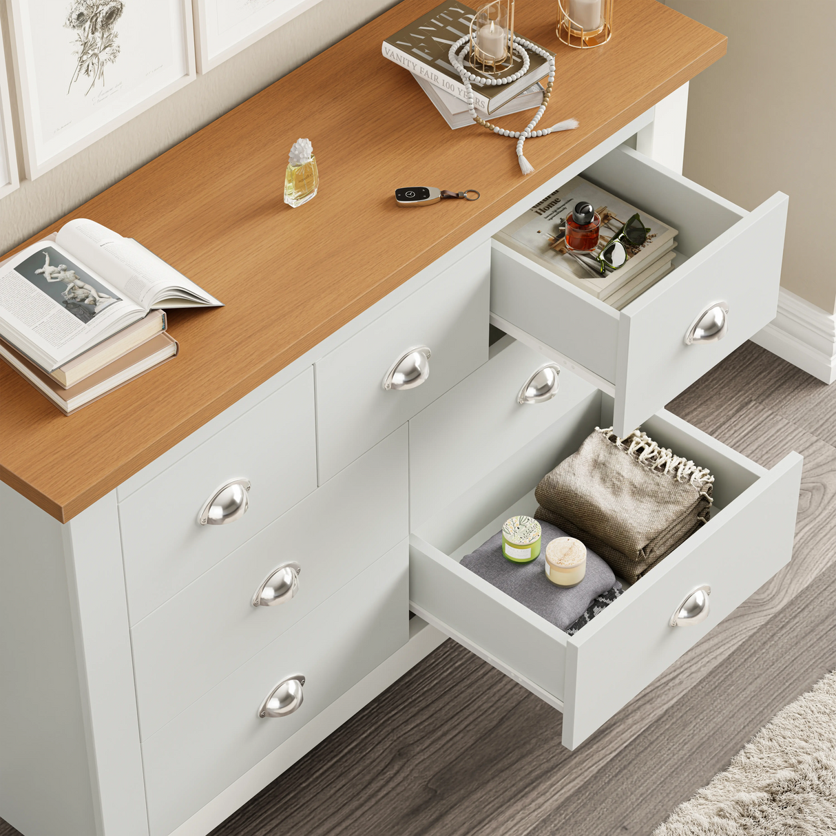 7 Drawer Wide Chest of Drawers with a wooden top and white body, featuring silver cup handles and open drawers showing folded clothes and accessories.