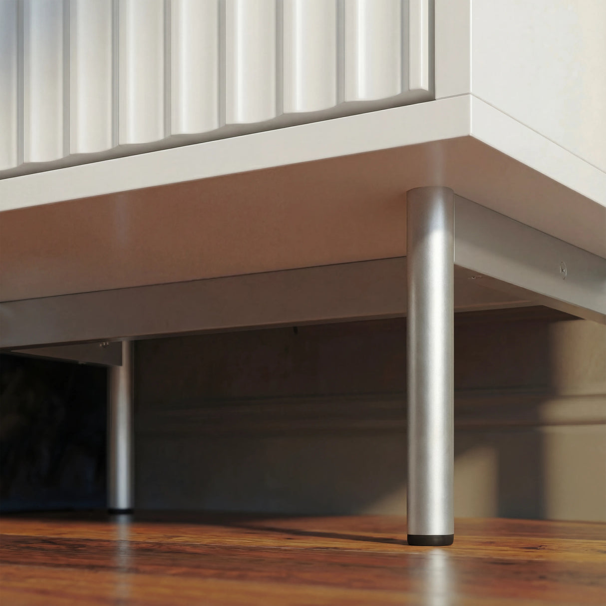 White bedside table base corner with slim silver metal legs placed on a wooden flooring
