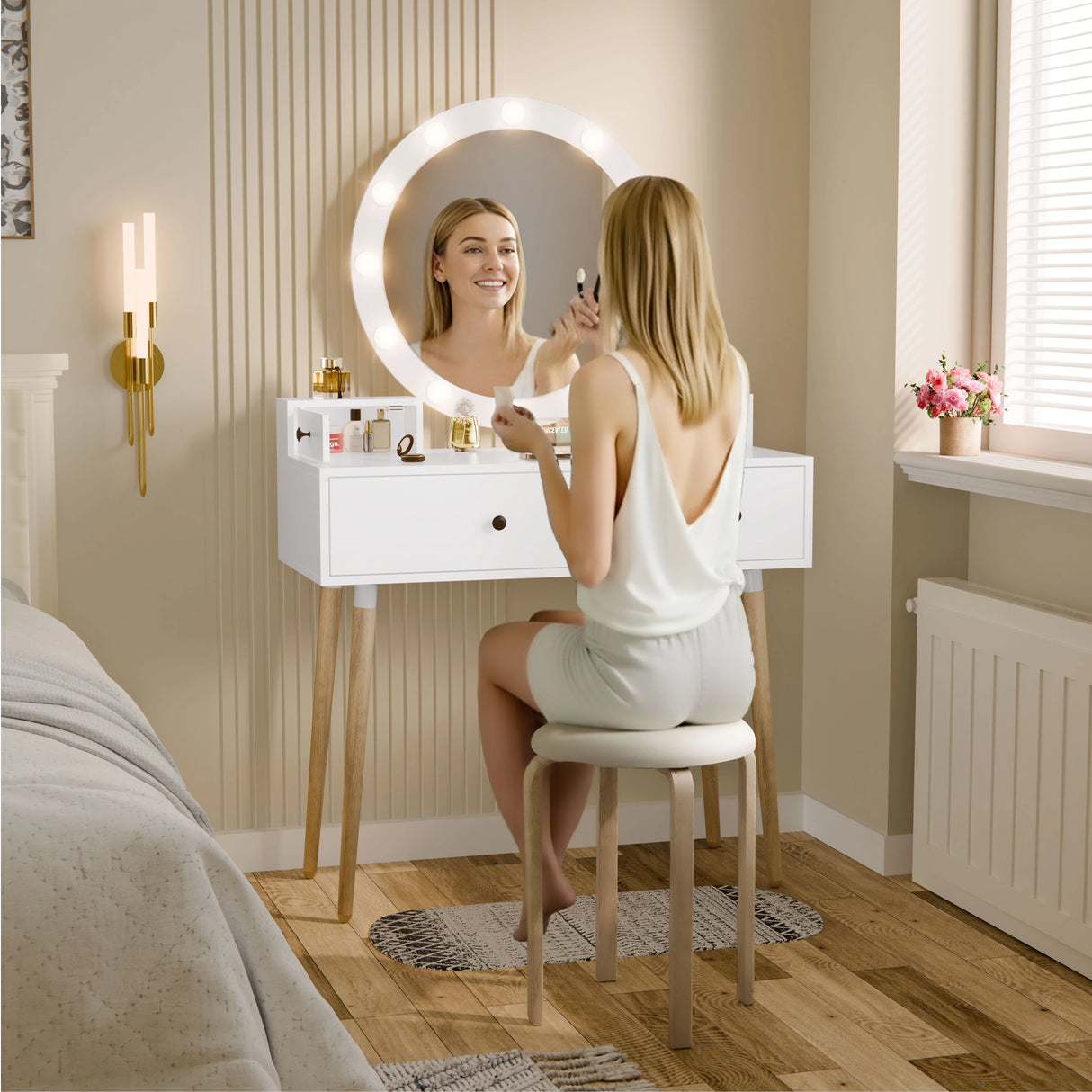 Woman using a handheld mirror in front of a white vanity with a round lighted mirror.