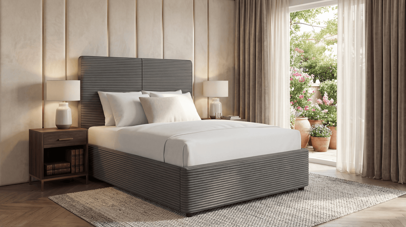Double ottoman bed in grey with white bedding, placed beside a nightstand and large windows with garden view