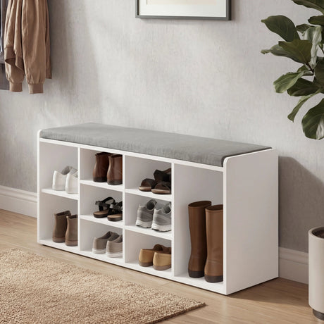 White shoe storage bench with shoes in a room with a plant and framed picture.