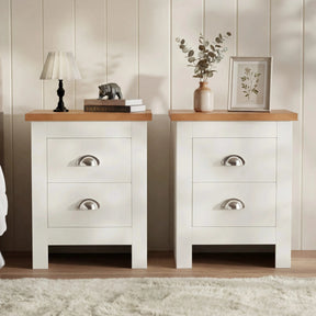 [White] Pair of white bedside table pair on rug, oak tops, cup handles, lamp and books left, vase and frame right
