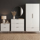 White bedroom furniture set including a wardrobe, chest of drawers, and bedside storage unit placed in a modern room