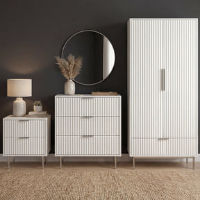 White bedroom furniture set including a wardrobe, chest of drawers, and bedside storage unit placed in a modern room