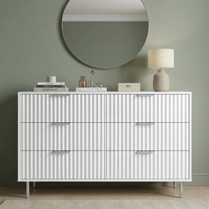 [White] dresser with decorative items against a green wall placed in a natural light room