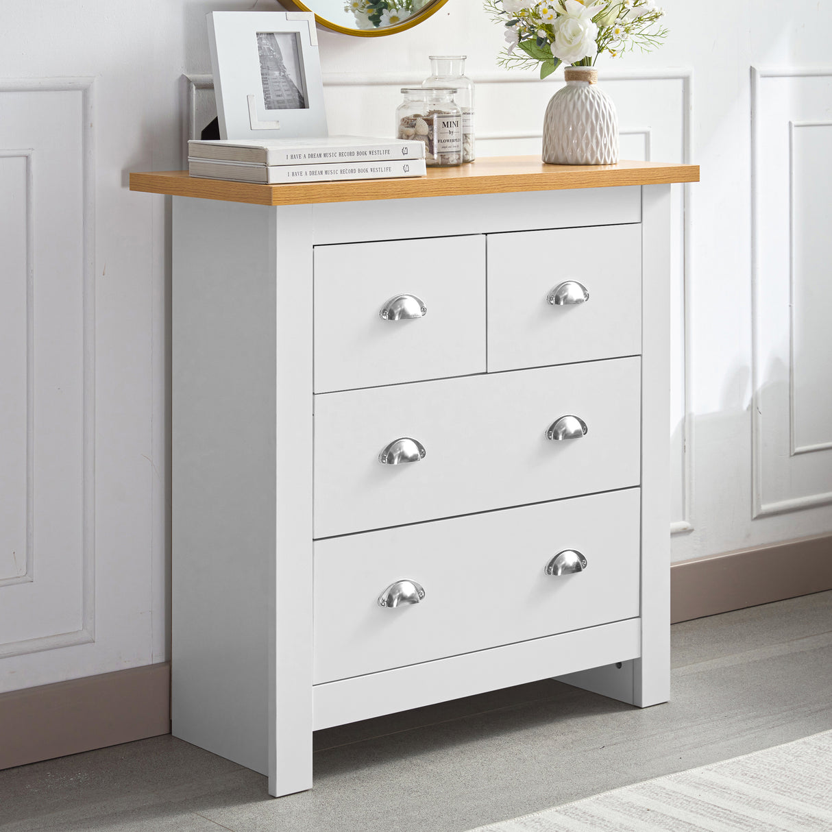 White 6-drawer chest of drawers with a wooden top, decorated with books and a vase with flowers.