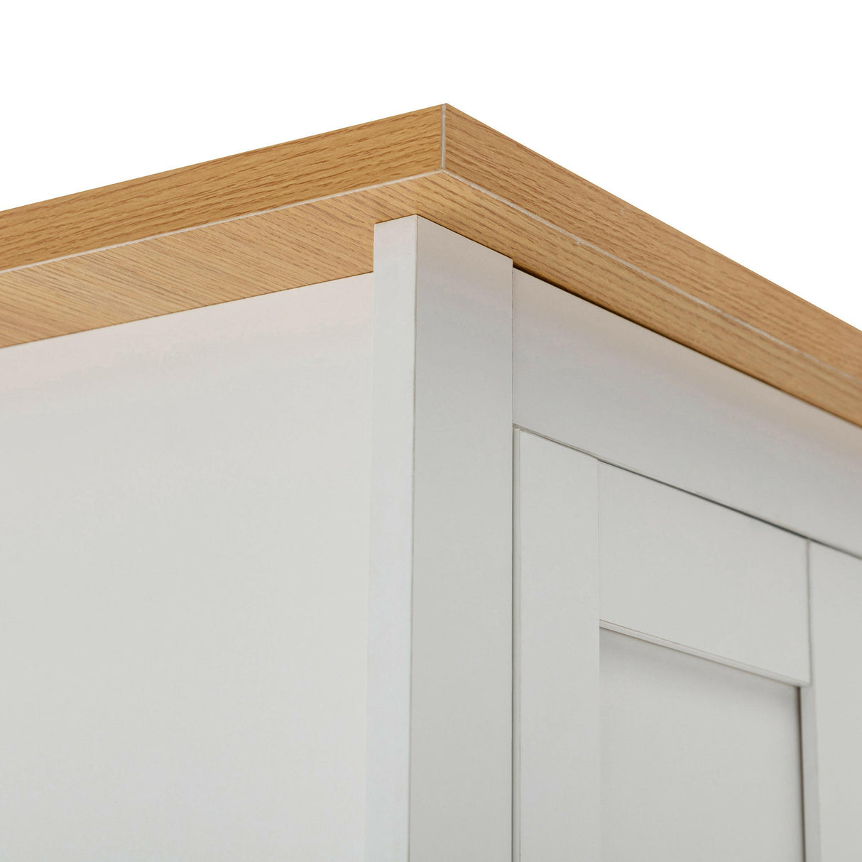 Close-up of the corner of a white wardrobe with a light oak wood finish top.