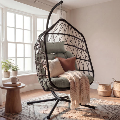 Hanging egg chair with cushions and a blanket in a room with a window and small table.