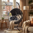 Round Garden Hanging Egg Chair placed in a sunlit living room corner with plush cushions and blanket, great for indoor comfort and decor.