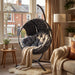 Round Garden Hanging Egg Chair placed in a sunlit living room corner with plush cushions and blanket, great for indoor comfort and decor.