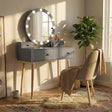 Dressing table with drawers and Hollywood mirror makeup vanity desk in grey with wooden legs, paired with cushioned chair in cozy bedroom setting.
