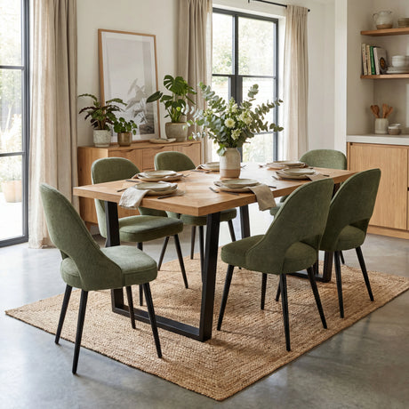 A modern dining area with a wooden table surrounded by 6 green chairs. The table is set with plates, cutlery and flowers.