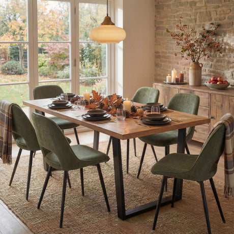A open dining room setup featuring a dining table with green chairs, adorned with autumn decorations like leaves and candles.