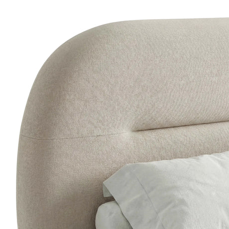 Close-up view of the beige bed frame's headboard, highlighting its soft fabric and unique design