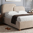 [King | Beige] A beige upholstered bed frame with a tall rounded headboard and matching footboard, shown dressed in white bedding with a dark brown throw blanket