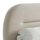 Close-up view of the beige king size bed's headboard which thick padding upholstery and light linens
