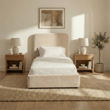 Front view of beige velvet single ottoman storage bed centred between bedside tables in a light neutral interior